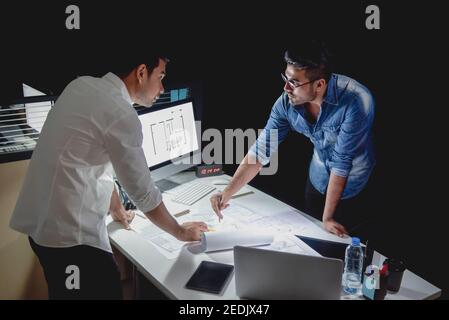 Asian architect team staying late at night in office discussing floor plan design project at meeting table Stock Photo