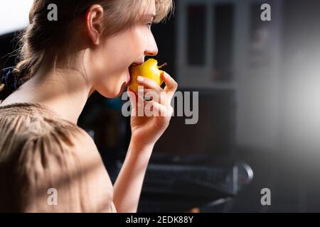 Healthy eating promotion. A young blonde looks out the window, lit by daylight. Profile photo of a happy girl savoring breakfast. Stock Photo