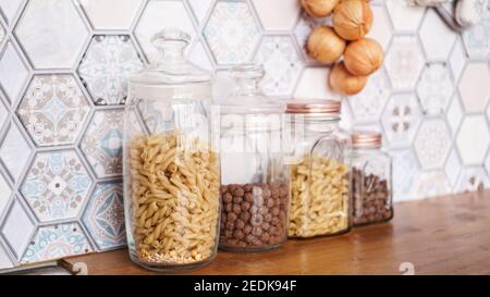 Pasta in glass jars. Pasta on a wooden countertop in a modern bright kitchen. Stock Photo