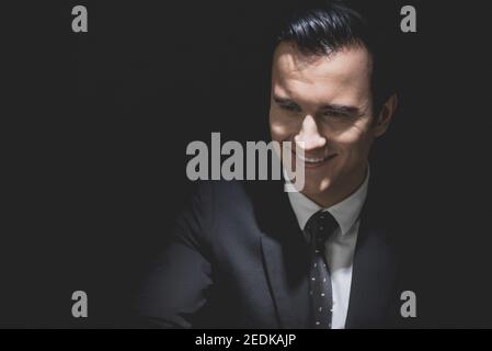 Man in formal business suit with smiling cunning face staring at interlocutor in dark shadow Stock Photo