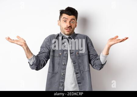 I dont know. Clueless young man shrugging and looking confused, have nothing to say, standing unaware on white background Stock Photo