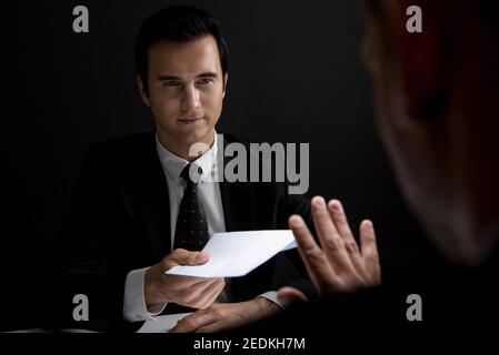 Businessman rejecting money in white envelope offered by his partner in shadow, anti bribery and corruption concept Stock Photo