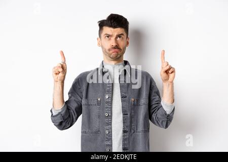 Hesitant Sad frowning guy pointing and looking up, standing hesitant on white ...