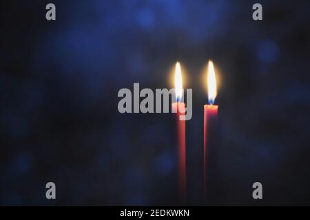 Burning candles in Darkness. Two red candles on black background with blue light bokeh. Stock Photo