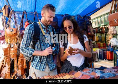 Couple tourists looking at leather products in shopping stall at outdoor market in Bangkok Thailand on vacations Stock Photo