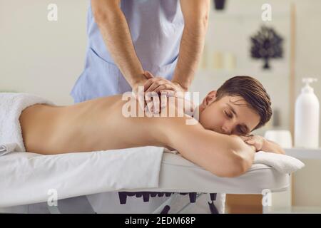 Young man with eyes closed enjoying procedure of medical massage from professional masseur Stock Photo