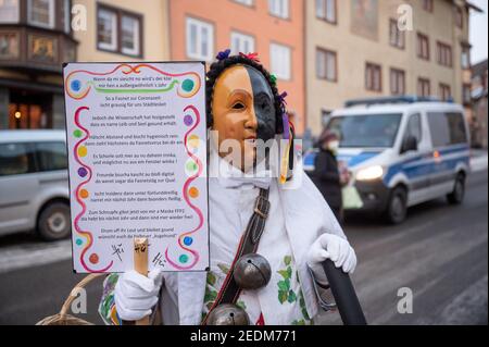 Rottweil, Germany. 15th Feb, 2021. A fool stands in front of a police car on Shrove Monday with a poem about 'Fasnet in Corona time'. Due to the Corona pandemic, the Narrensprung was officially cancelled, but some fools were still on the road. The Rottweiler Narrensprung is one of the highlights of the Swabian-Alemannic carnival and one of the traditional parades in the southwest. Credit: Sebastian Gollnow/dpa/Alamy Live News Stock Photo