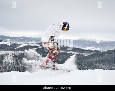 Full length of alpine skier skiing on fresh powder snow in winter mountains. Man freerider in winter ski pants making jump while sliding down snow-covered slopes. Concept of winter sports.