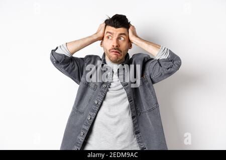 Guy looking aside in panic, stare at logo nervous and alarmed, having trouble, holding hands on head, standing on white background Stock Photo