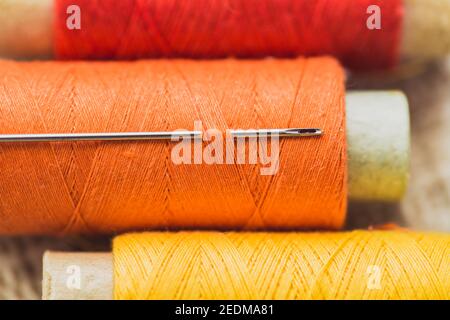 Sewing needle in a spool of thread in orange - tailor material and tools Stock Photo