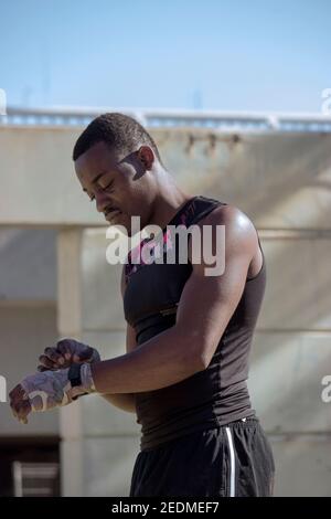 Young black professional boxer in black t-shirt bandages his hands ready to box during the Covid 19 pandemic outdoors.Boxing and Training Concept 2021 Stock Photo