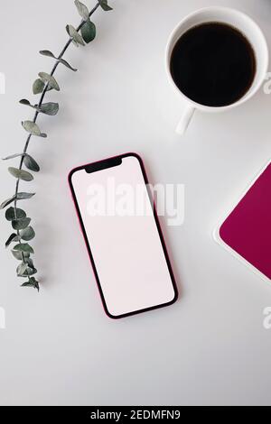 Smartphone, green eucalyptus branch and coffee on white table Stock Photo