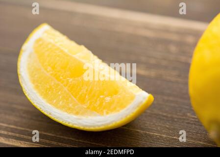 Wedge of fresh juicy ripe yellow lemon on wood table, closed up shot Stock Photo