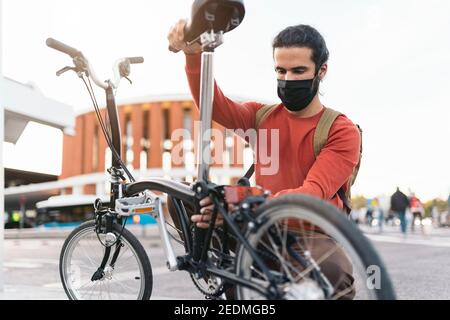Stock photo of man wearing face mask folding his bike in the street. Stock Photo