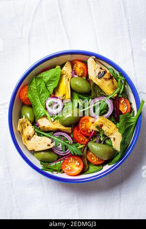 Green salad with artichokes, tomatoes and olives in a white bowl. Stock Photo
