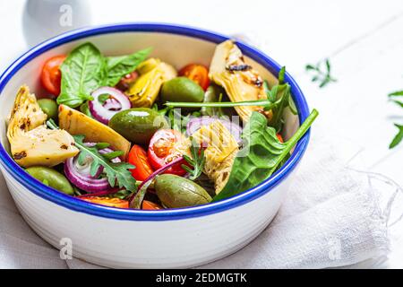 Green salad with artichokes, tomatoes and olives in a white bowl. Stock Photo