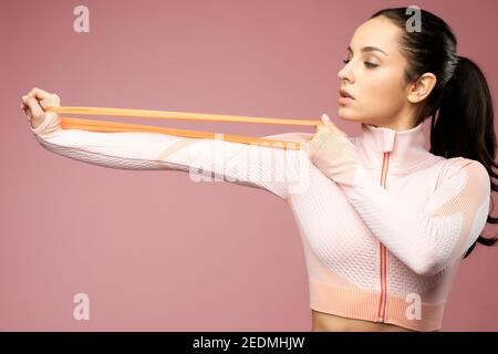 Attractive sporty lady doing exercise with elastic resistance band. Isolated on pink background Stock Photo