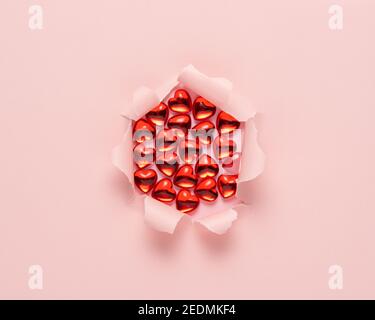 Vivid pink ripped paper with red glass hearts on pink background. Minimal abstract love concept. Stock Photo