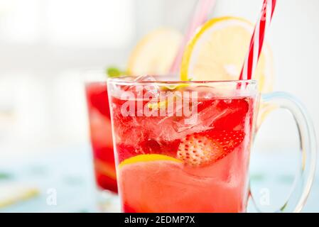 Colorful refreshing drinks for summer, cold strawberry lemonade juice with ice cubes in the glasses garnished with sliced fresh lemons Stock Photo