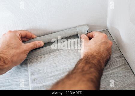 The master mounts a plastic skirting board on the laminate - fastening with screws to the wall - home repair Stock Photo