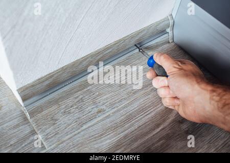 The master mounts a plastic skirting board on the laminate - fastening with screws to the wall - home repair Stock Photo