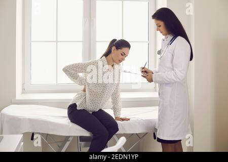 Unhappy woman complaining about backache sitting on examination bed at doctor's office Stock Photo