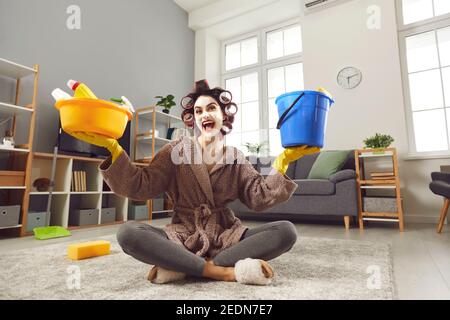 Funny energetic young housewife sitting on floor and holding plastic pail and tub Stock Photo