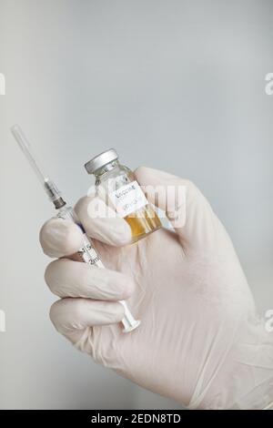 Vertical close up of doctors hand holding covid vaccine and syringe against white , copy space Stock Photo