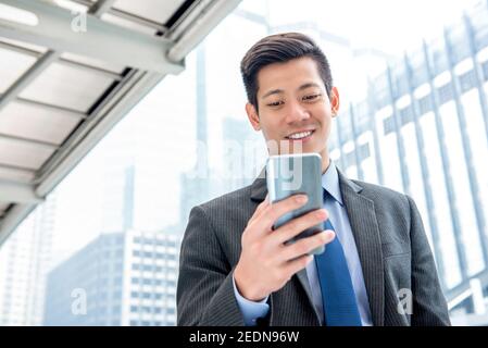 Young handsome Asian businessman  using mobile phone surfing internet searching for online information on the go Stock Photo