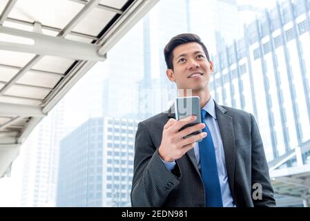 Young handsome Asian businessman  using mobile phone outdoors on the go Stock Photo