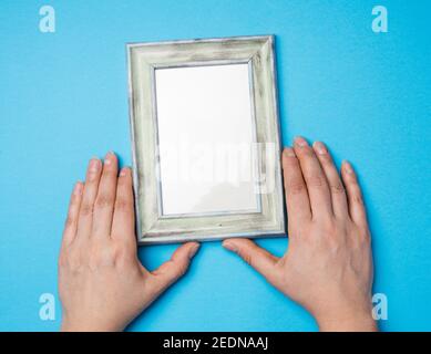 two female hands holding a rectangular blank wooden frame, blue background Stock Photo