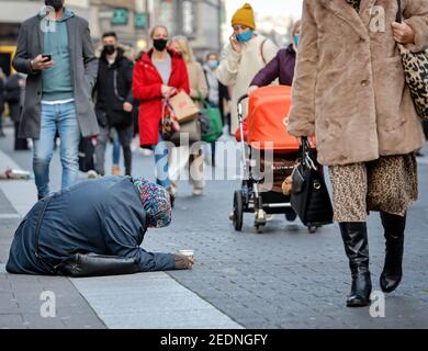 27.11.2020, Duesseldorf, North Rhine-Westphalia, Germany - Beggar woman sits on the pavement in the pedestrian zone in Duesseldorf's old town during t Stock Photo