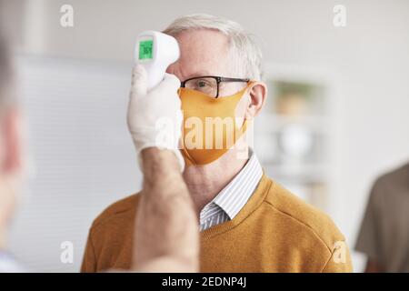 Shot of unrecognizable doctor checking temperature of senior man wearing mask in line at clinic or hospital, copy space Stock Photo