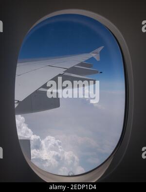 Beautiful view of the blue sky and white puffy clouds outside, as seen from the window of an aircraft. Stock Photo