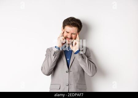 Business man in suit having headache, grimacing and touching head, suffer migraine, standing sick on white background Stock Photo