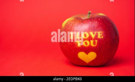 Valentine's Day themed apple with I Love You message and a heart symbol placed on a red background Stock Photo