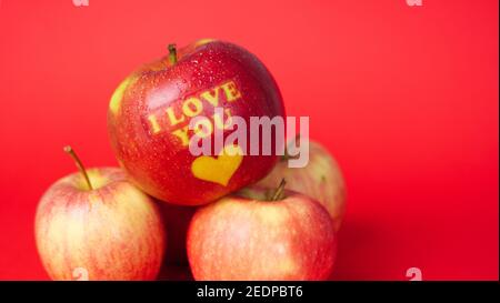 Valentine's Day themed apple with I Love You message and a heart symbol covered in water droplets and placed on a red background Stock Photo