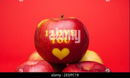 Valentine's Day themed apple with I Love You message and a heart symbol placed on a red background Stock Photo