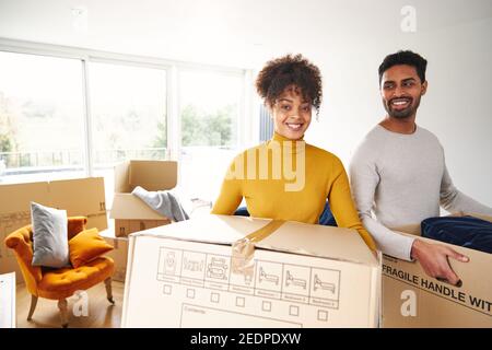 Portrait of young mixed ethnicity couple carrying removal boxes into new home on moving day together Stock Photo