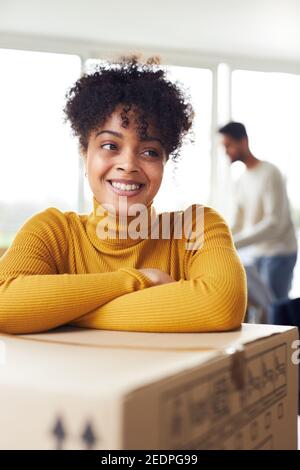 Portrait of young mixed ethnicity couple moving into new home with woman leaning on removal box and smiling at camera Stock Photo