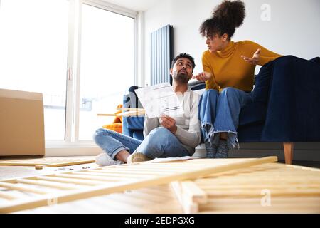 Young couple sitting on sofa in lounge at home arguing whilst reading instructions for flat pack furniture assembly Stock Photo