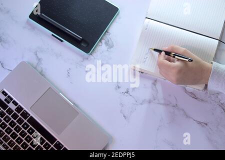 Top view unrecognizable man writing daily planner, computer and graphic tablet on marble desk background. Small Business Owner Concept 2021. Stock Photo