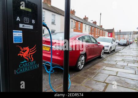 Cardiff, Wales, UK - February 14th 2021: A red Tesla, electric car (EV) uses a charging point, provided by Cardiff Council, in a residential street. Stock Photo