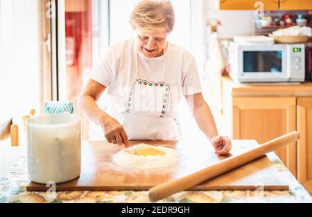Happy woman preparing handmade receipt at house kitchen - Local food concept with home made italian pasta preparation - Warm bright backlight filter Stock Photo
