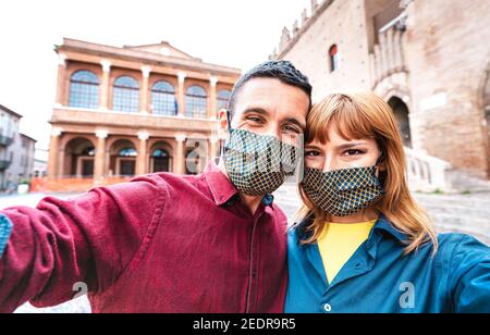 Happy girlfriend and boyfriend in love taking selfie covered by face mask at old town tour - New normal life style travel concept with tourist couple Stock Photo