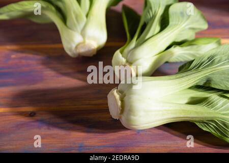 Fresh green bok choy or pac choi chinese cabbage on a colored wooden background. Hard light, contrast. Side view, close up, selective focus. Stock Photo