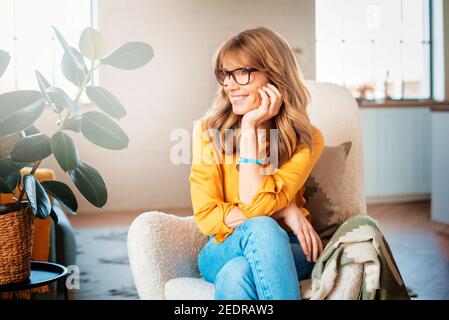 Portrait shot of happy middle aged woman relaxing in the armchair at home. Stock Photo