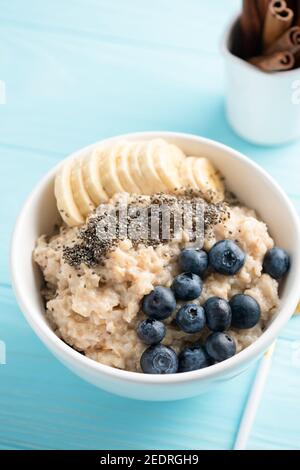 Oatmeal porridge with banana slices and blueberries in bowl on blue backround, copy space for text or design Stock Photo