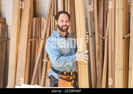 Young craftsman as a carpenter apprentice carries boards in the wood store of the joinery Stock Photo