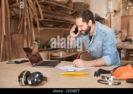 Young handyman man using laptop computer while talking to customer on the phone Stock Photo
